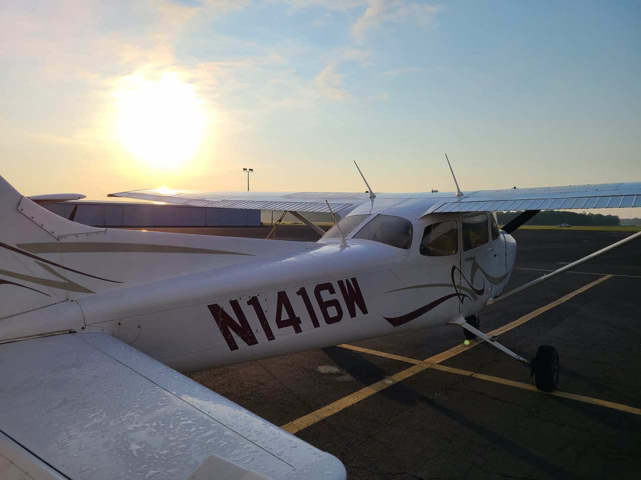 The tail and fuselage of a white Cessna with registration N1416W on a tarmac during a bright, hazy sunrise.